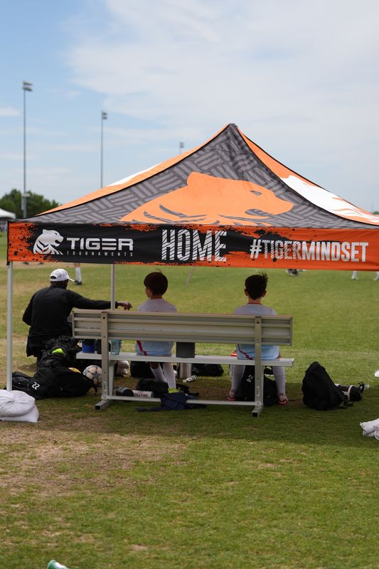 Orange and charcoal HOME team canopy with players seated on a bench at the field