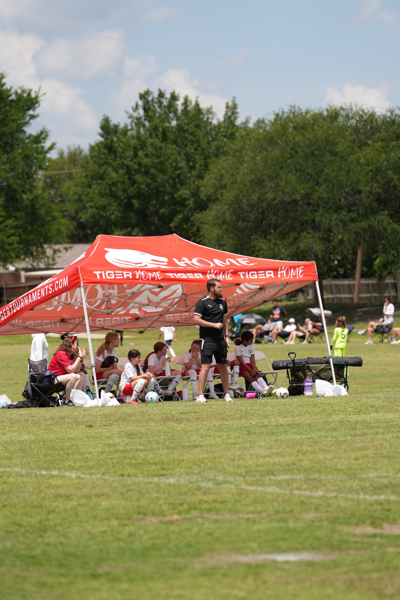 Red branded team canopy with players seated at a soccer tournament